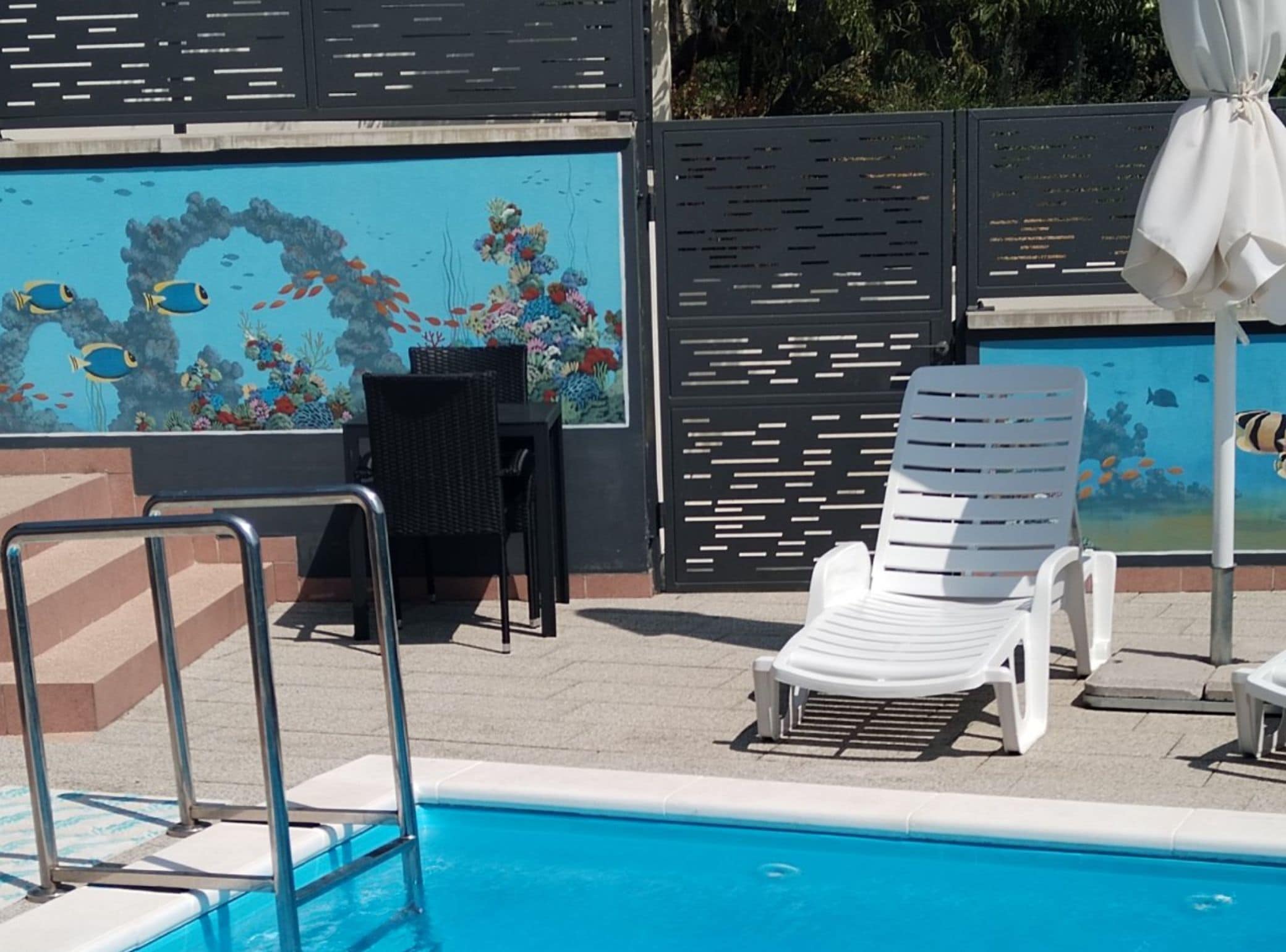 A pool area with a mural of fish and coral, a white lounge chair, and a table with chairs.