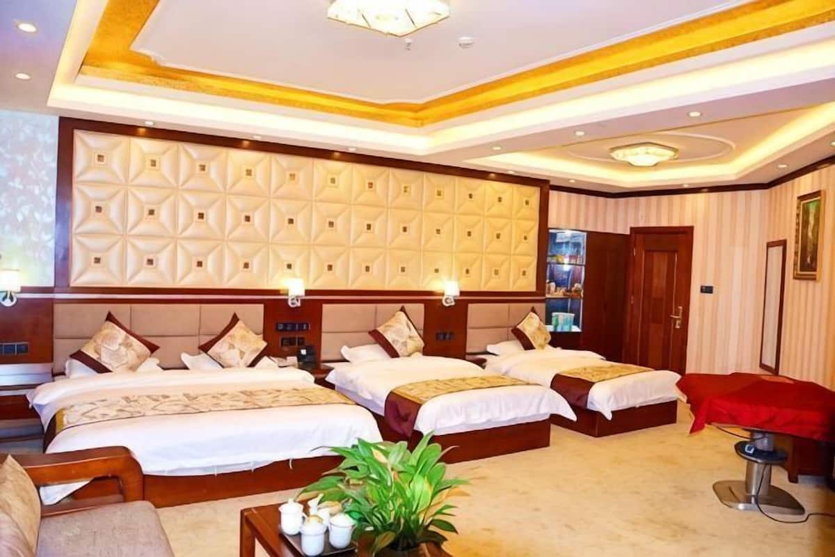 Een hotelkamer met drie bedden, een massagestoel, een televisie en een minibar.