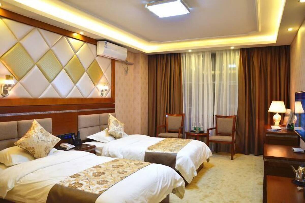 Two single beds with matching headboards and decorative panels, a nightstand with a lamp, and a seating area with a chair.