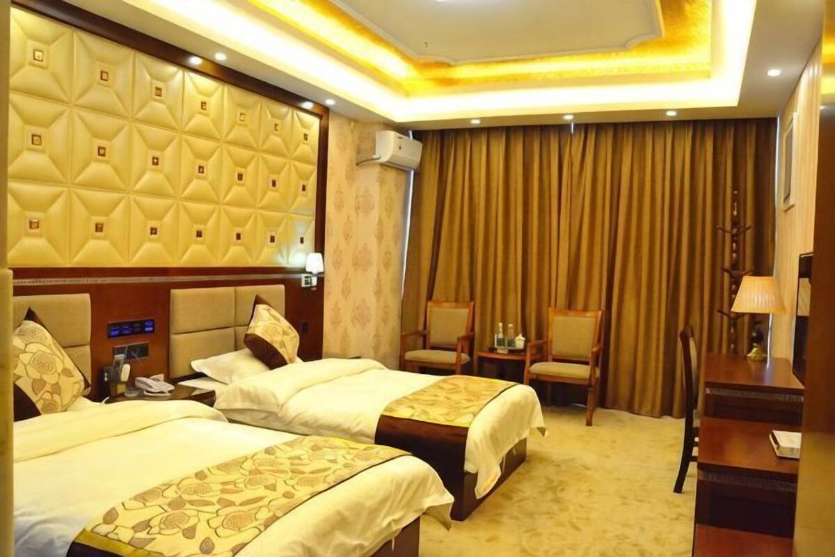 Een hotelkamer met twee bedden, een hoofdbord met een geometrisch patroon, een tafeltje met een lamp en een stoel.