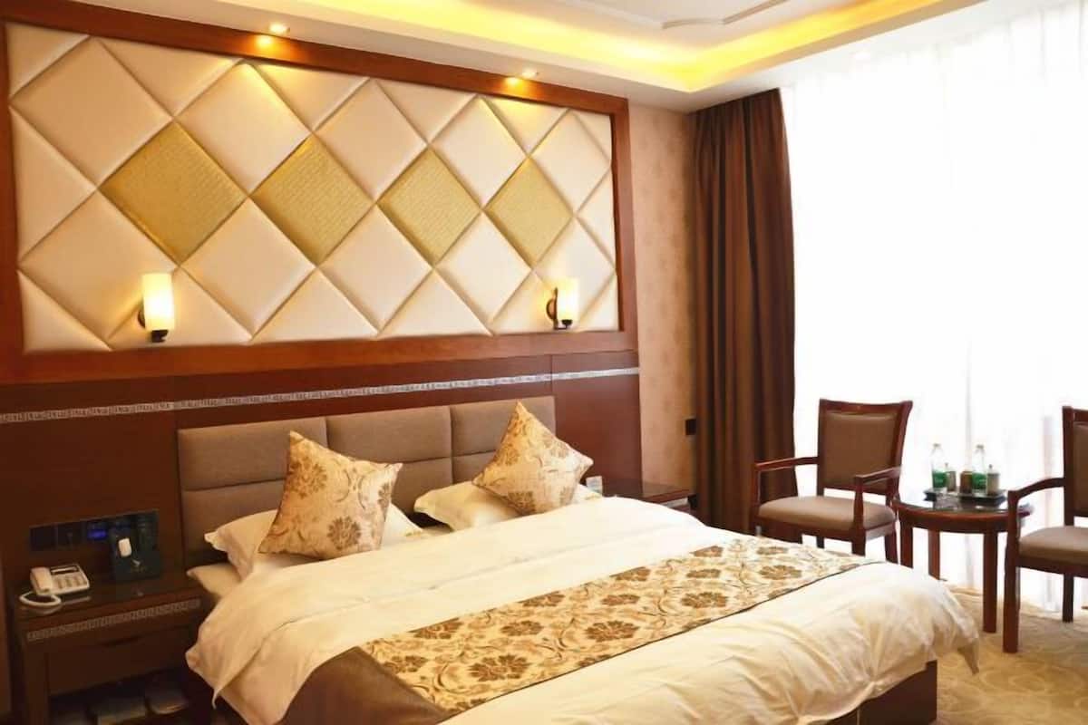 Hotelkamer met een groot bed, een hoofdbord met een diamantmotief, twee bedlampen, een nachtkastje met een telefoon en een kleine tafel met stoelen.