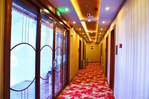 Un couloir d’hôtel avec des portes en verre, une moquette rouge et un plafond doté d’un éclairage encastré.