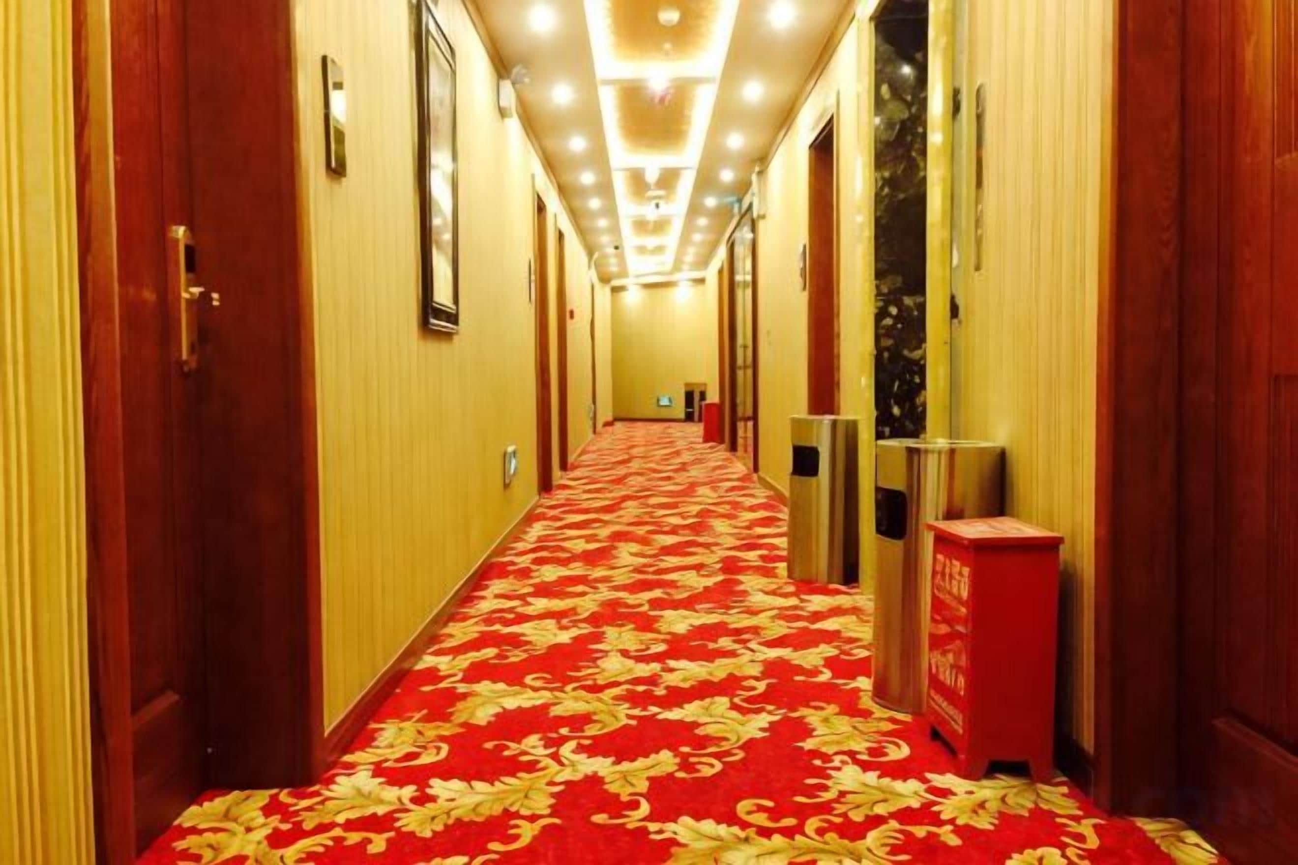 Un pasillo de hotel con alfombra roja, puertas y un bote de basura.