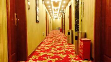 Un pasillo de hotel con alfombra roja, puertas y un bote de basura.