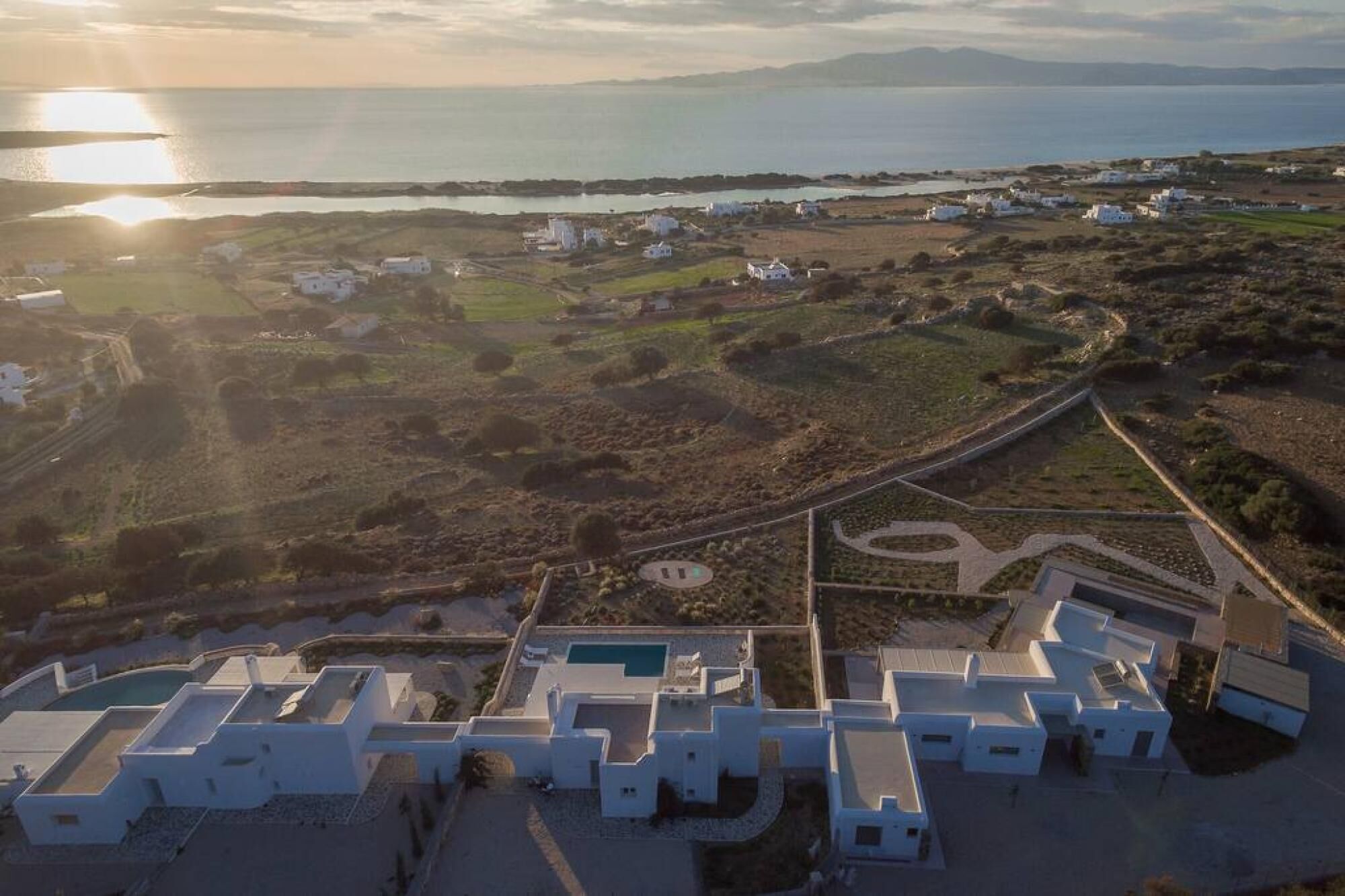 Vista aerea di una zona costiera con edifici bianchi, una strada e un corpo d'acqua sullo sfondo.