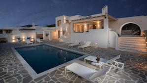 En modern villa med pool, stengolv och utomhusmöbler.