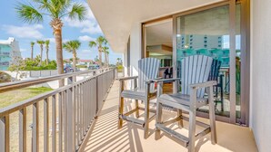 A balcony with two Adirondack chairs, a glass door leading to an indoor area, and palm trees in the background. - Beachfront 1st Floor | Heated Pool-Sherwin #107 (Daytona Beach Shores)