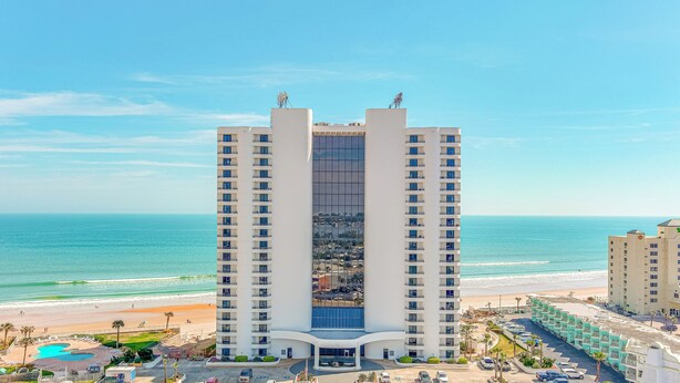 A high-rise hotel with a central glass facade, located near a beach with a clear view of the ocean. - Beachfront 1st Floor | Heated Pool-Sherwin #107 (Daytona Beach Shores)