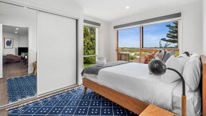 A bedroom with a large bed, a view of greenery, and a sliding door leading to another room. - Dune Views, Gas Fire and Pet friendly. (Ocean Grove)