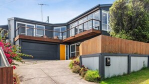 A modern two-story house with a garage, large windows, and a wooden deck. - Dune Views, Gas Fire and Pet friendly. (Ocean Grove)