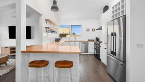 A modern kitchen with a wooden countertop, stainless steel appliances, and two bar stools. - Dune Views, Gas Fire and Pet friendly. (Ocean Grove)