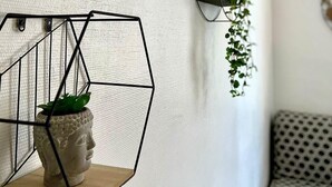 Une pièce avec un mur blanc à texture, une étagère métallique aux motifs géométriques sur laquelle repose une sculpture représentant une tête de Bouddha, et un canapé à motifs.