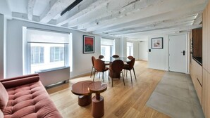 A spacious living area with a high ceiling, a dining table with chairs, a sofa, and a large window providing natural light. - 11.Flat 8 person St Lazare Galerie LaFayette 8ème (Paris)
