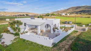 Una villa bianca con patio, circondata dal verde e da campi, con un panorama collinare.