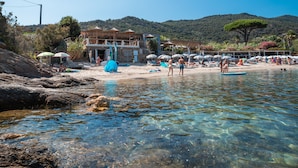 Une plage avec une eau claire, des parasols et un bâtiment à plusieurs étages.