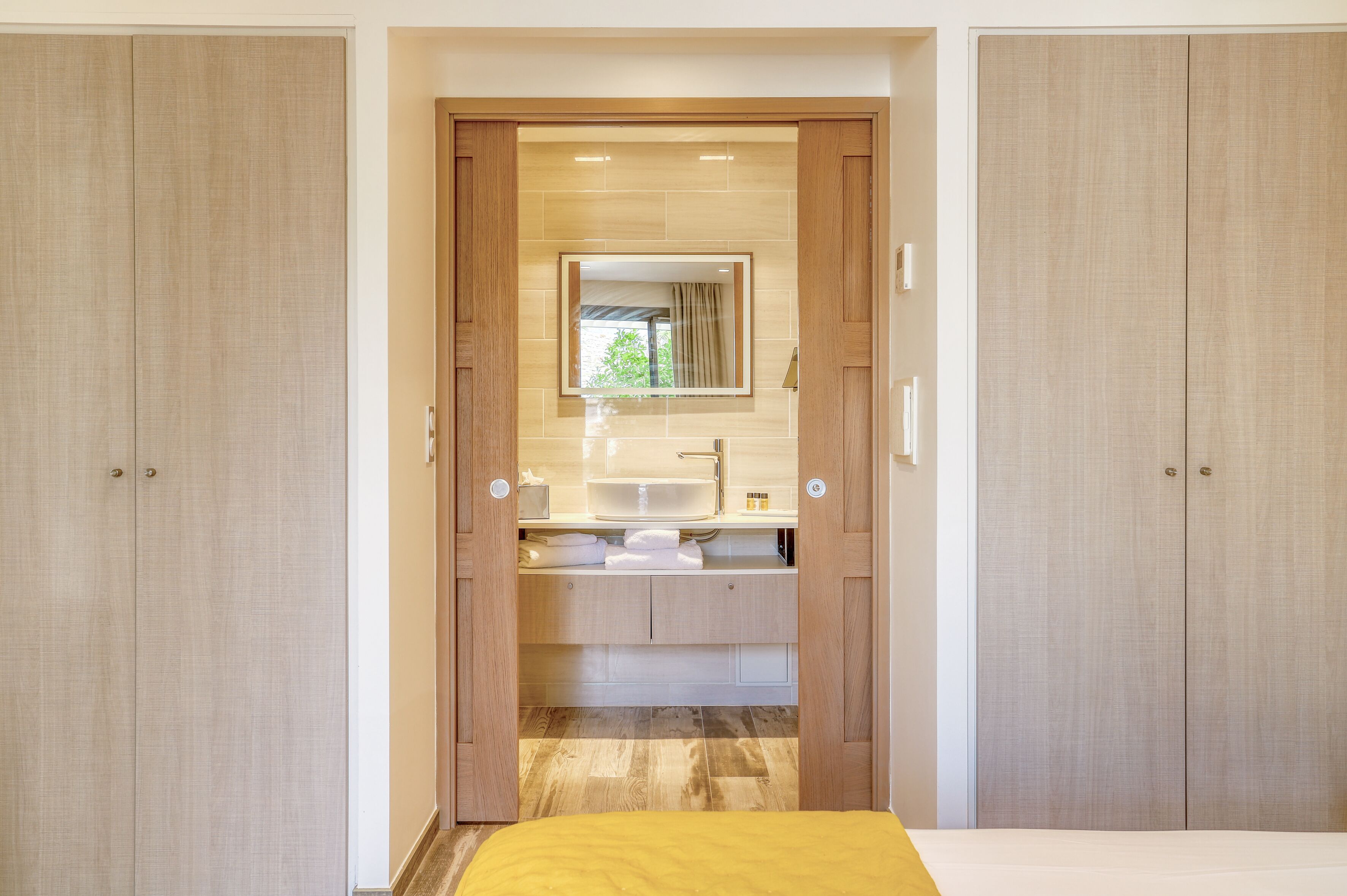 Une chambre moderne avec une armoire en bois, une coiffeuse intégrée dotée d’un miroir et un lit recouvert d’une couverture jaune.