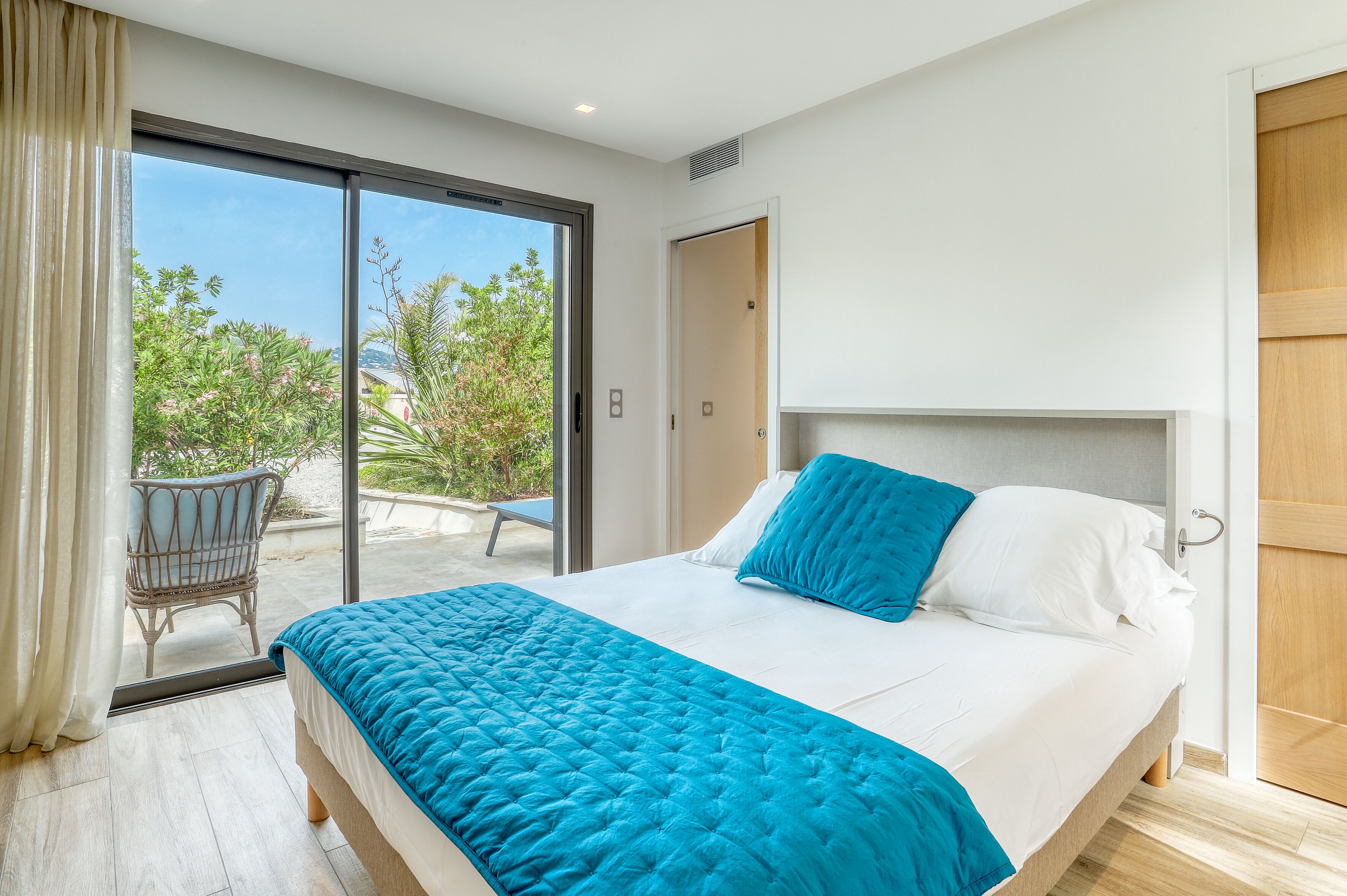 A bedroom with a bed, a chair, and a sliding glass door leading to an outdoor area.