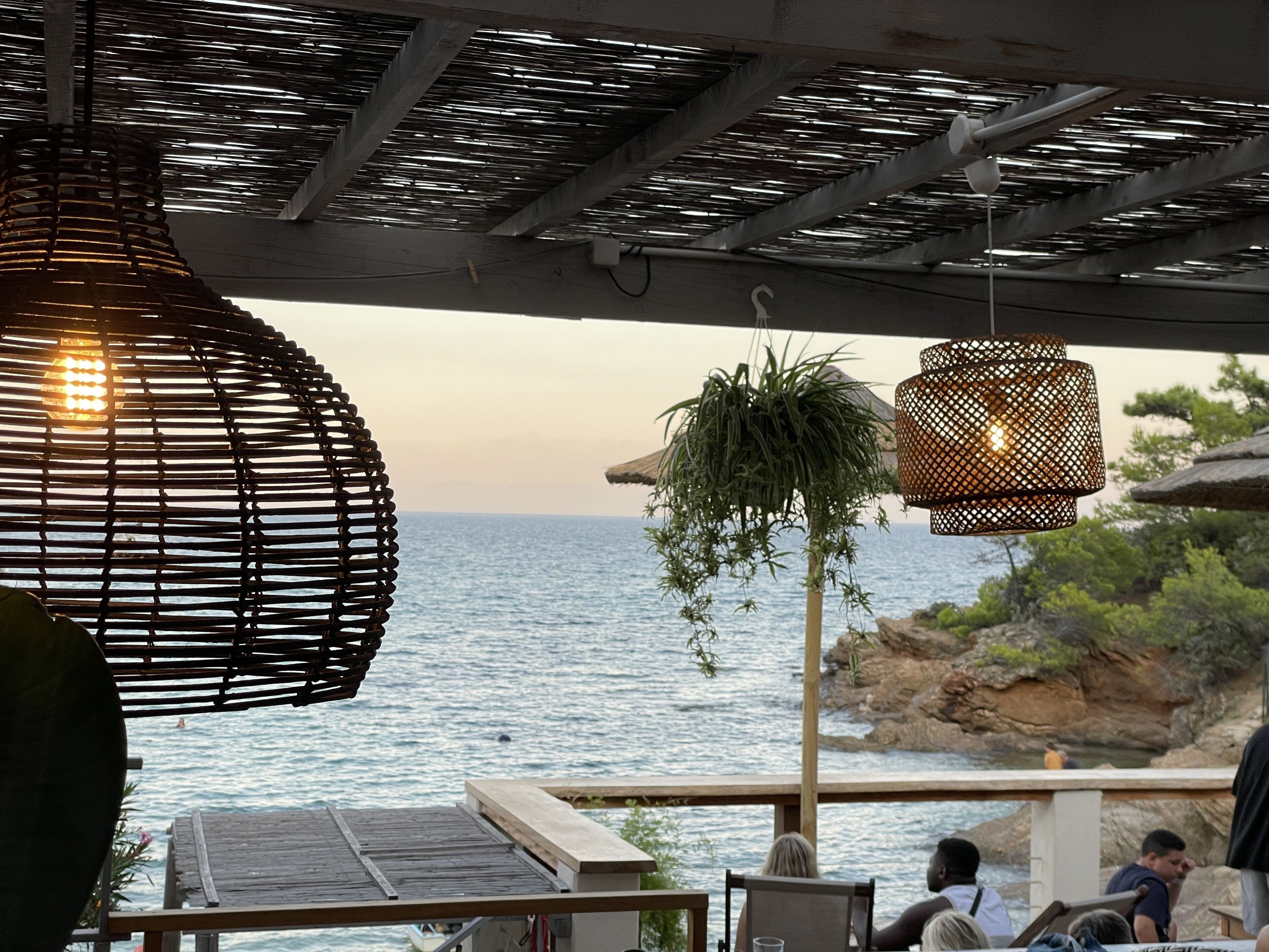 Un espace extérieur aménagé avec des sièges et offrant une vue sur la mer, agrémenté de lampes en osier et d’une terrasse en bois.