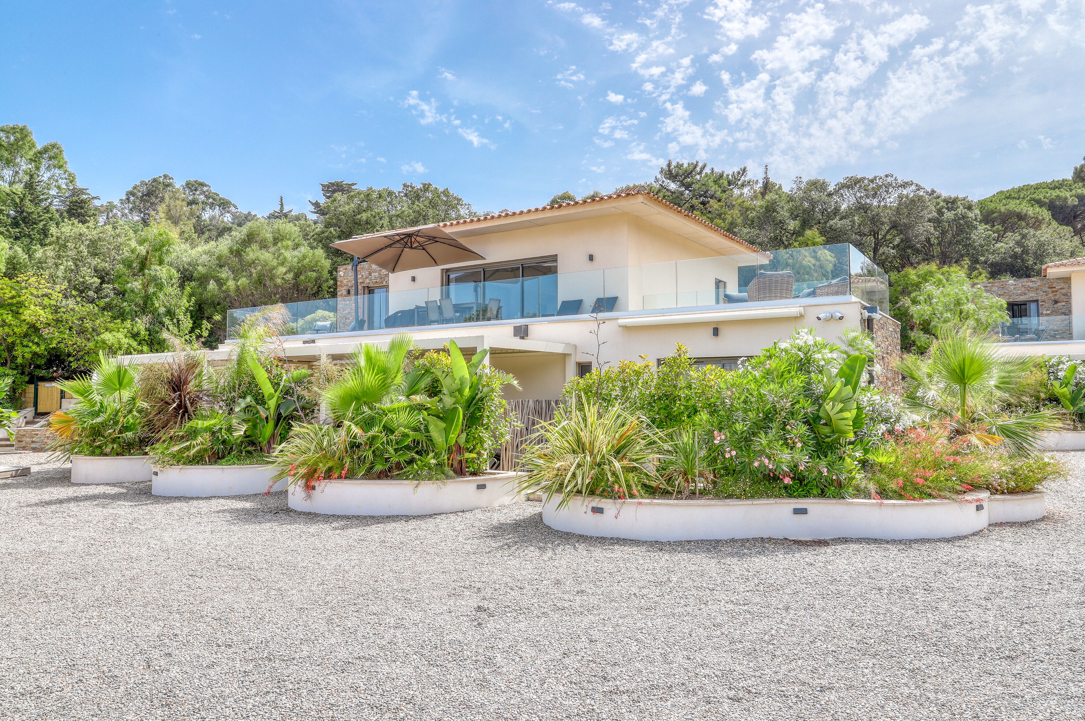 A modern villa with a glass balcony, surrounded by landscaped gardens and a clear sky.