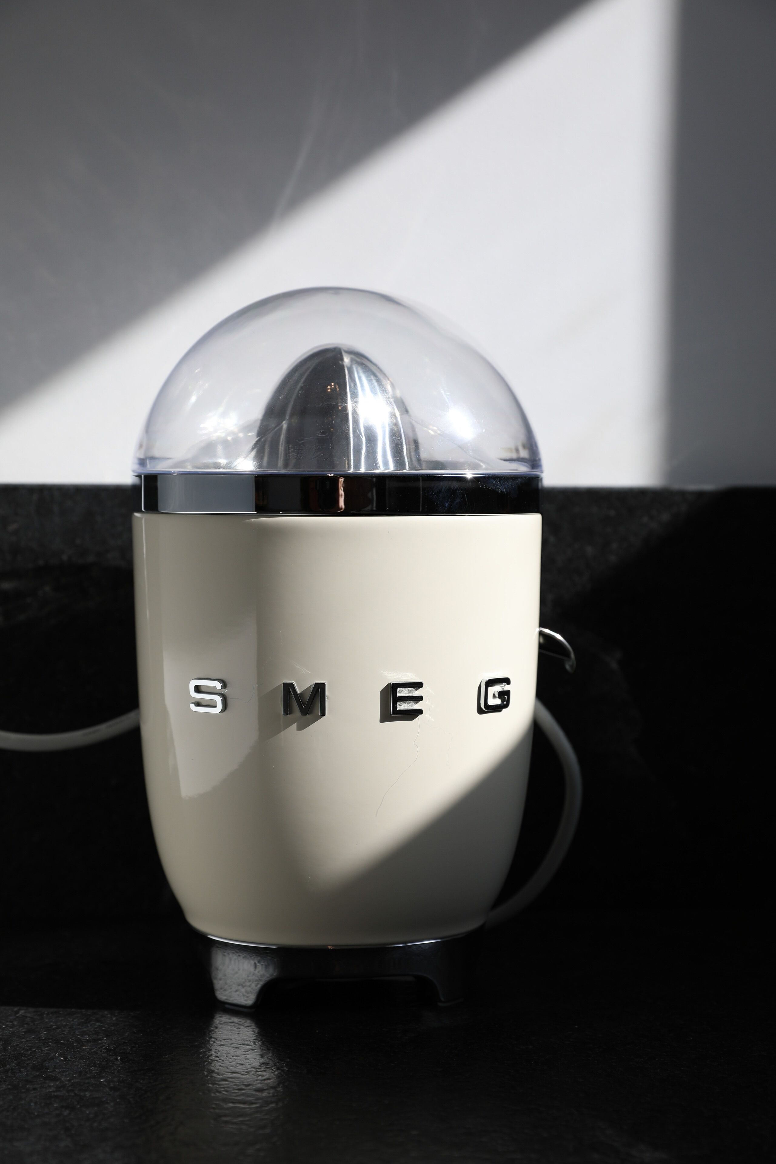 A white, vintage-style speaker with the brand name "SMEG" on its side, placed on a dark surface.