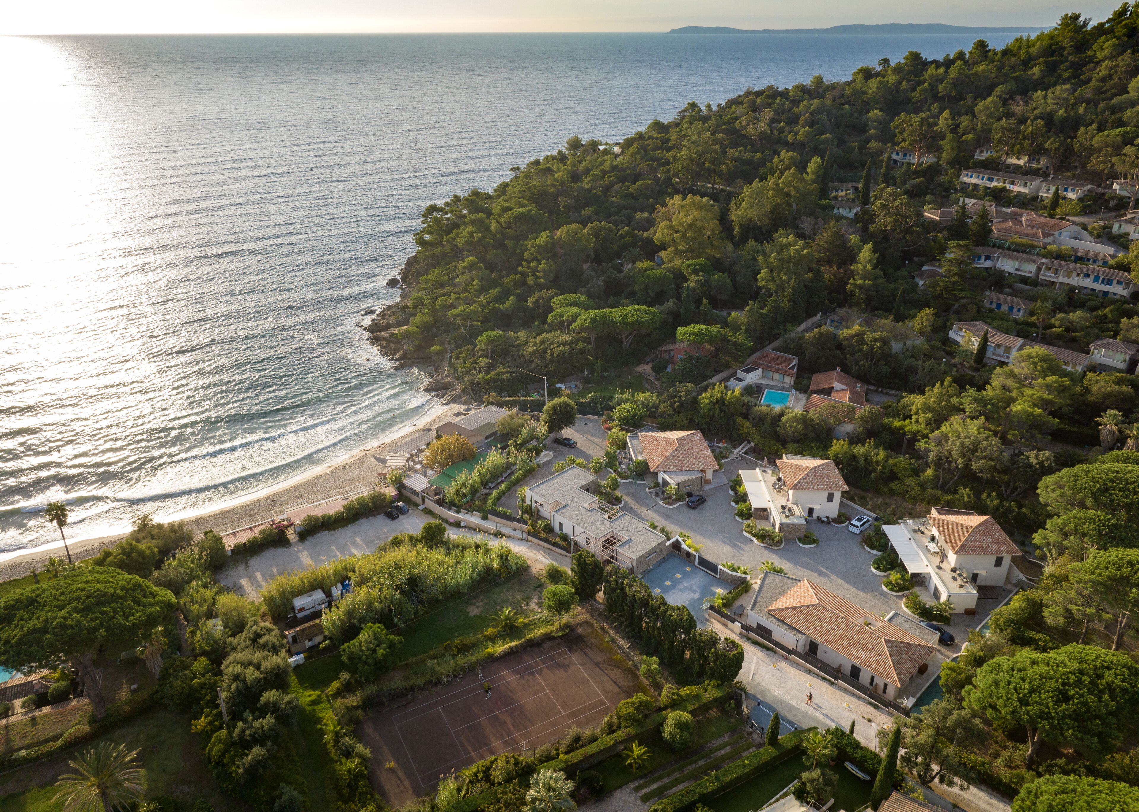 An aerial view of a coastal residential area with houses, a beach, and a tennis court.