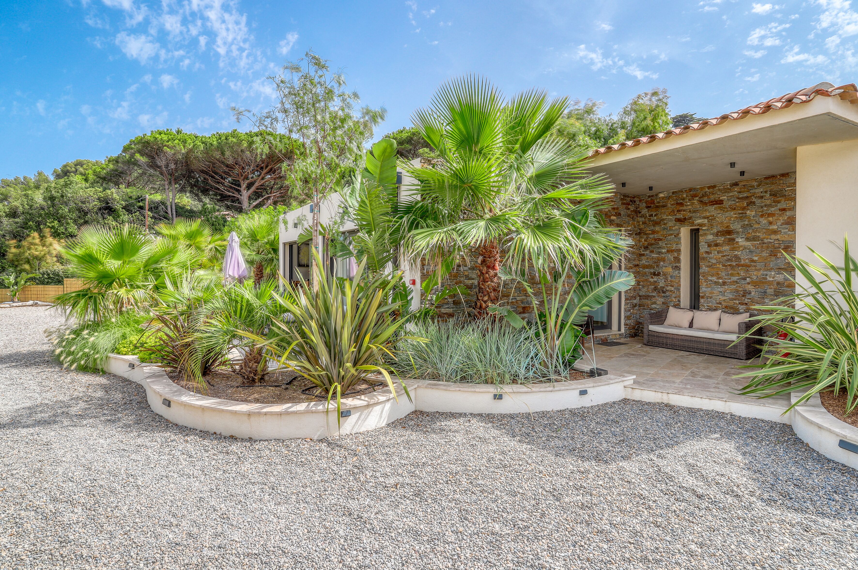 A garden with various plants and a stone building with a covered patio.