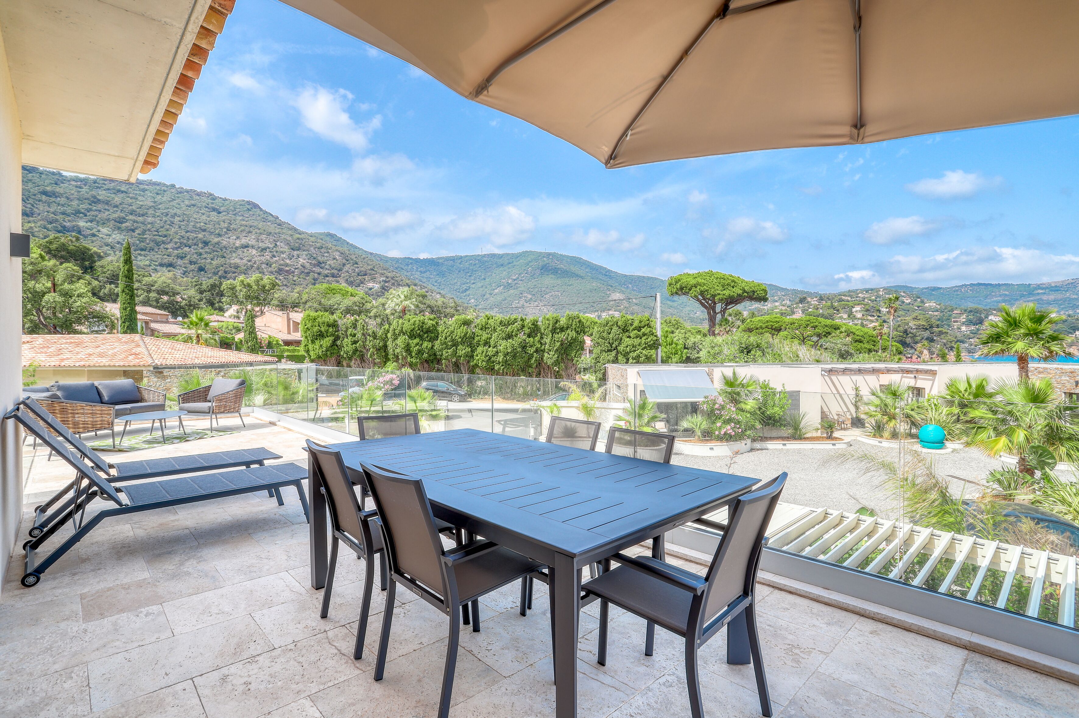 Una terraza con mesa y sillas, una tumbona y vistas a un paisaje montañoso.
