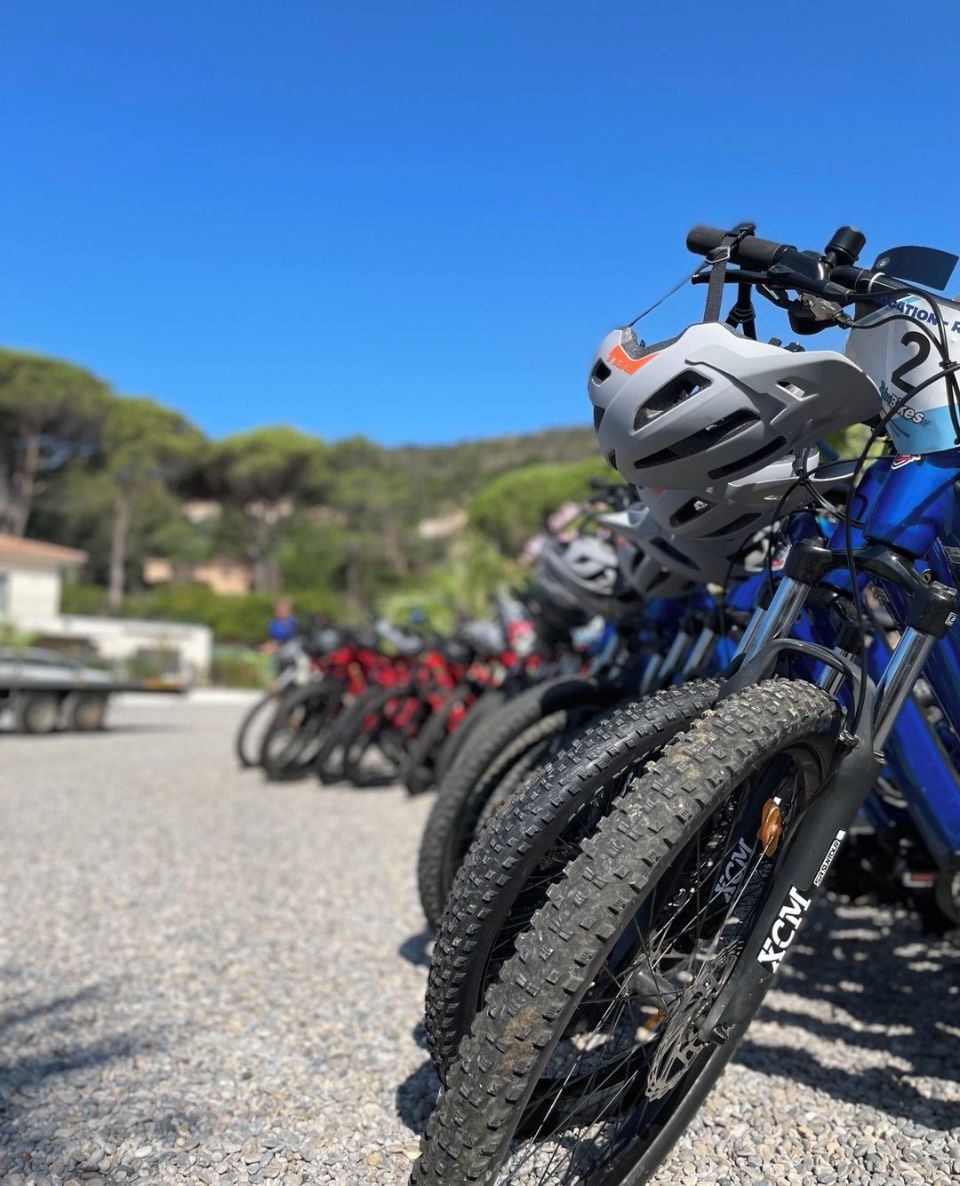 A row of bicycles with helmets, each marked with a number, parked on a gravel surface.