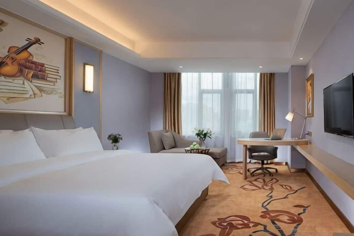 A hotel room with a large bed, a desk, a chair, a TV, and a window with curtains.