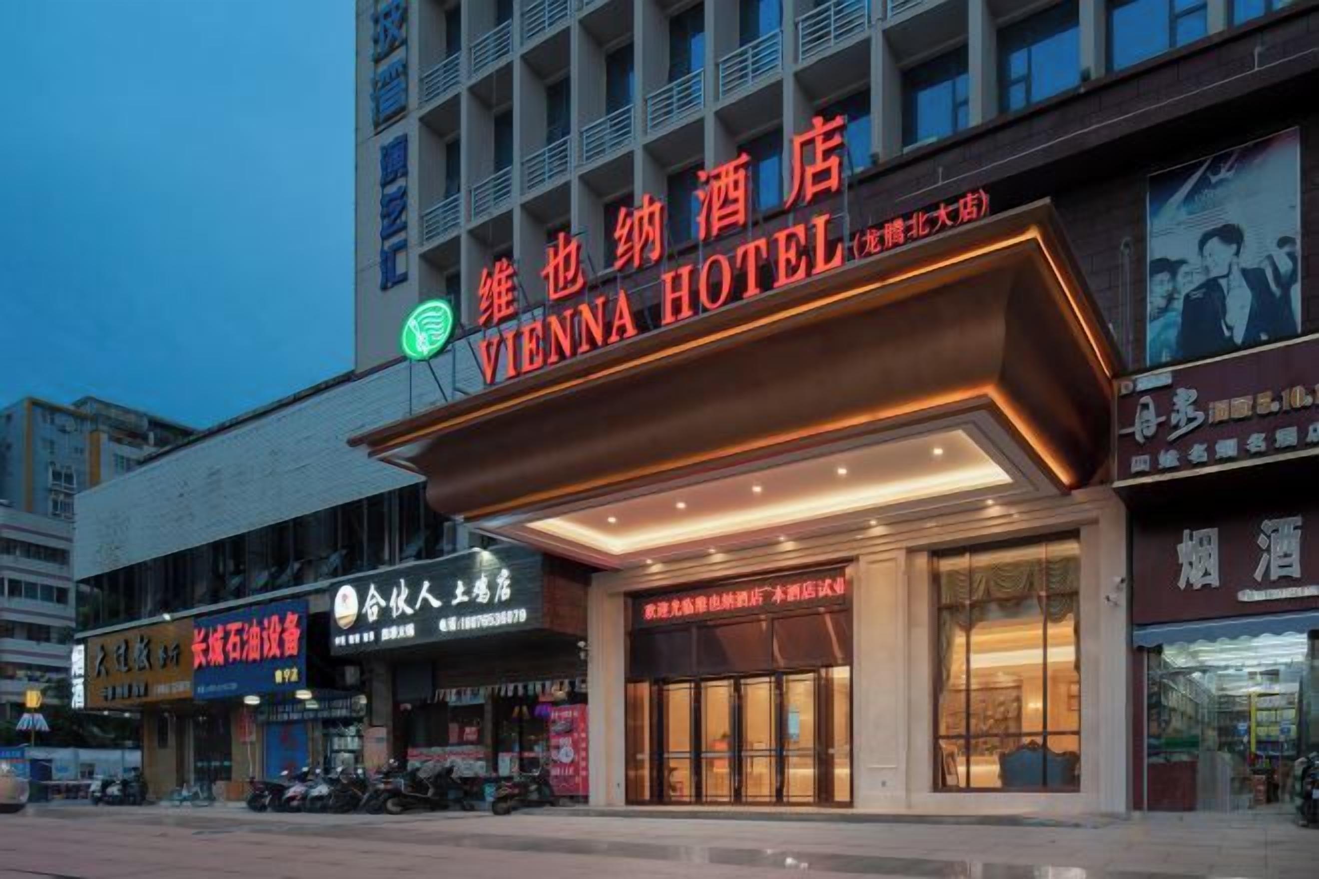 Un hotel con un letrero llamativo, una entrada amplia y un estacionamiento con varios coches.