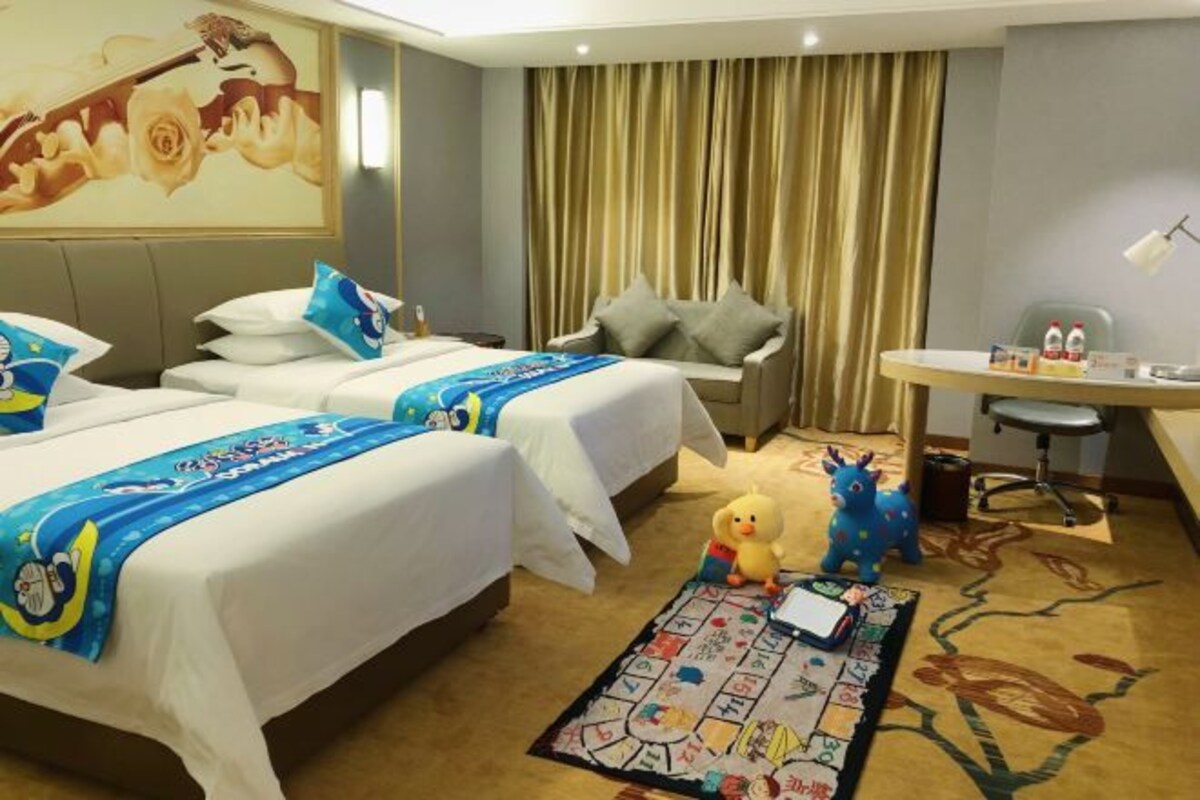 Une chambre d’hôtel avec deux lits, un bureau, une chaise, un jouet en peluche et un jeu de société posé sur le sol.