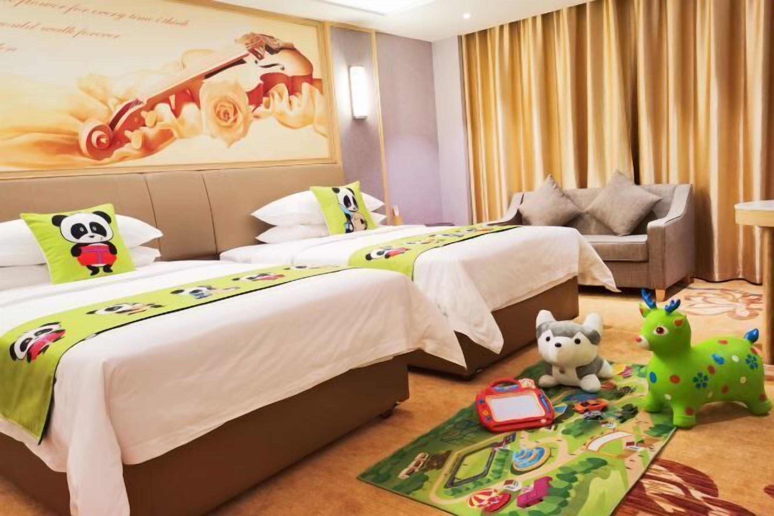 Ein Hotelzimmer mit zwei Betten, einem Schlafsofa, einem Kuscheltier und einer Kinderspielecke.