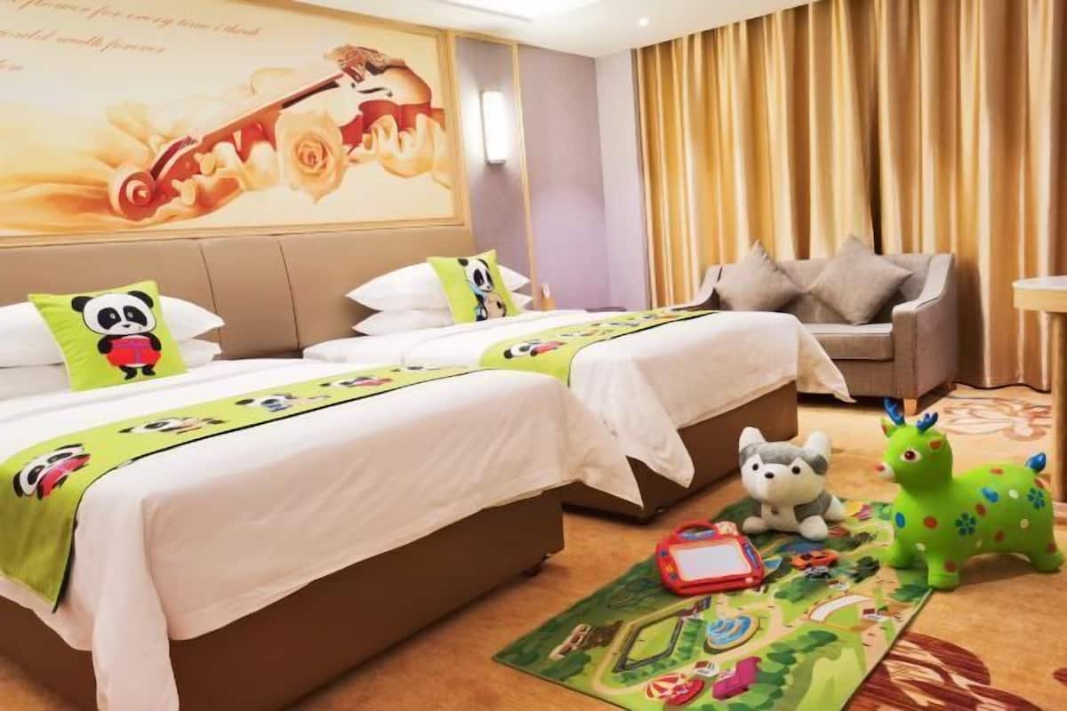 A hotel room with two beds, a sofa, a plush toy, and a children's play mat.
