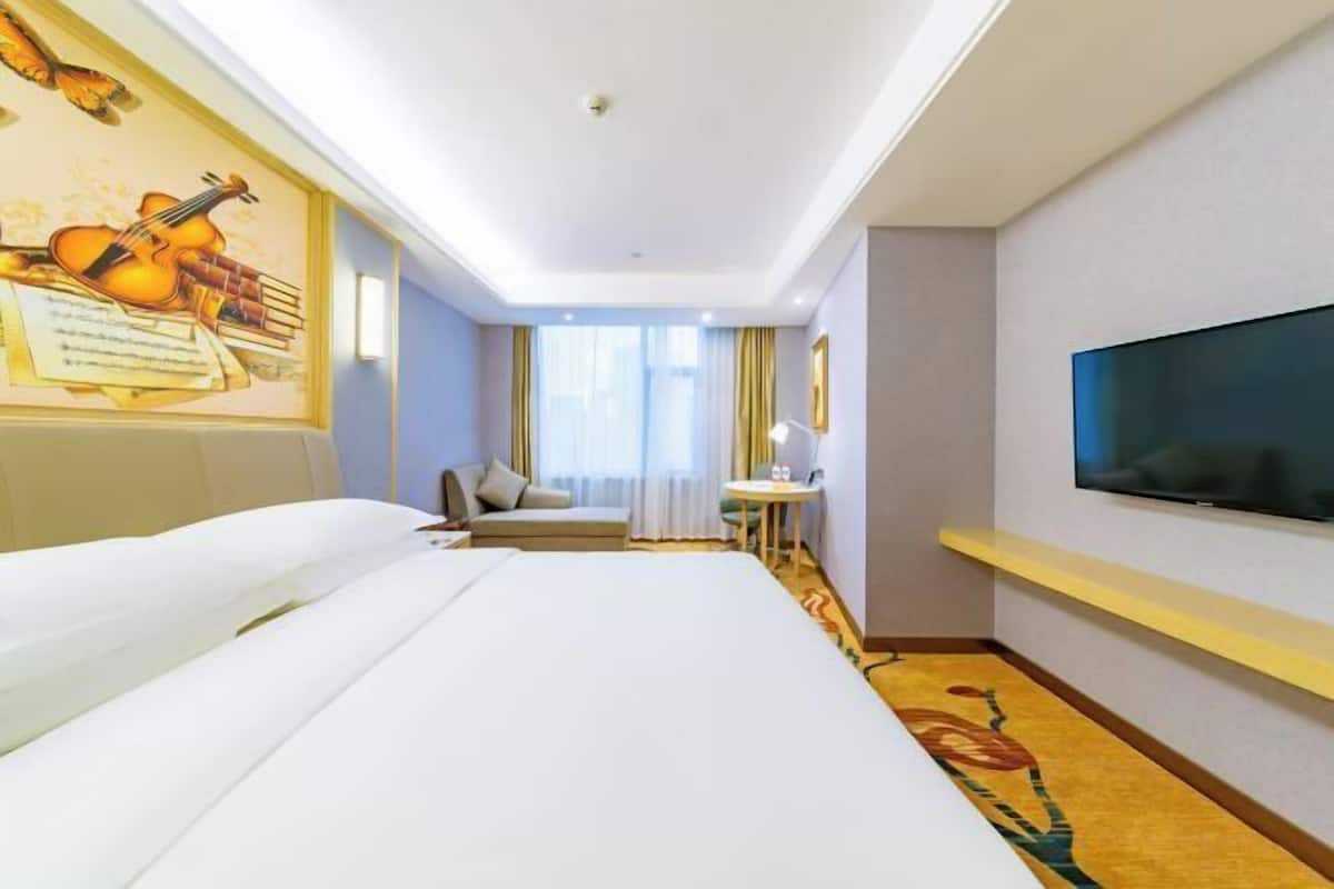 A hotel room with a bed, a desk, a chair, a television, and a wall with a framed picture.