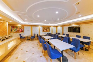 Une salle à manger d’hôtel avec des tables et des chaises, un comptoir de réception et un écran de télévision fixé au mur.