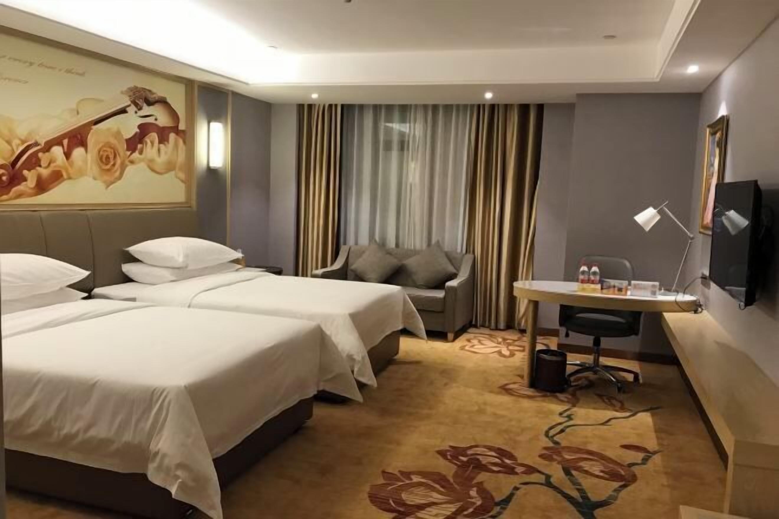 Ein Hotelzimmer mit zwei Betten, einem Schreibtisch, einem Sessel und einem Fernseher, sowie einem großen, blumigen Teppich.