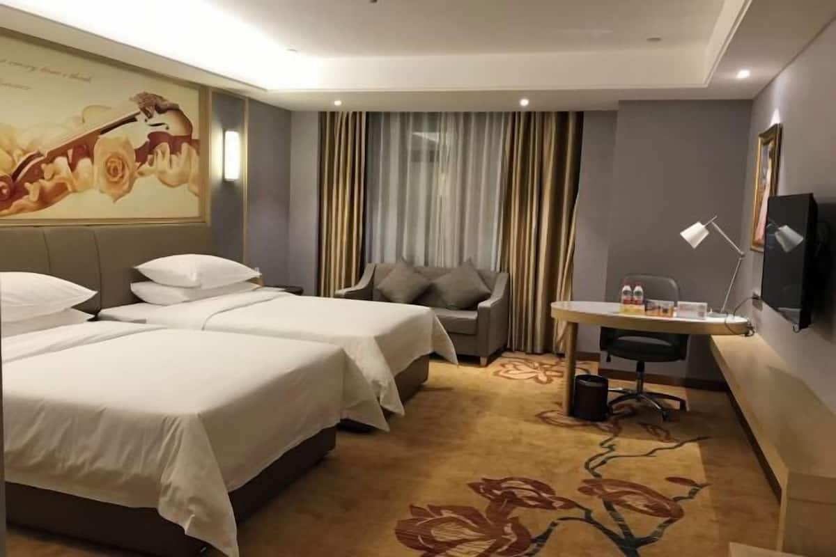 A hotel room with two beds, a desk, a chair, a television, and a large floral carpet.