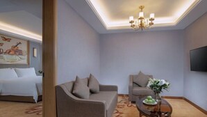 Quarto de hotel com uma cama, um sofá, uma mesinha com um vaso de flores e uma televisão na parede.