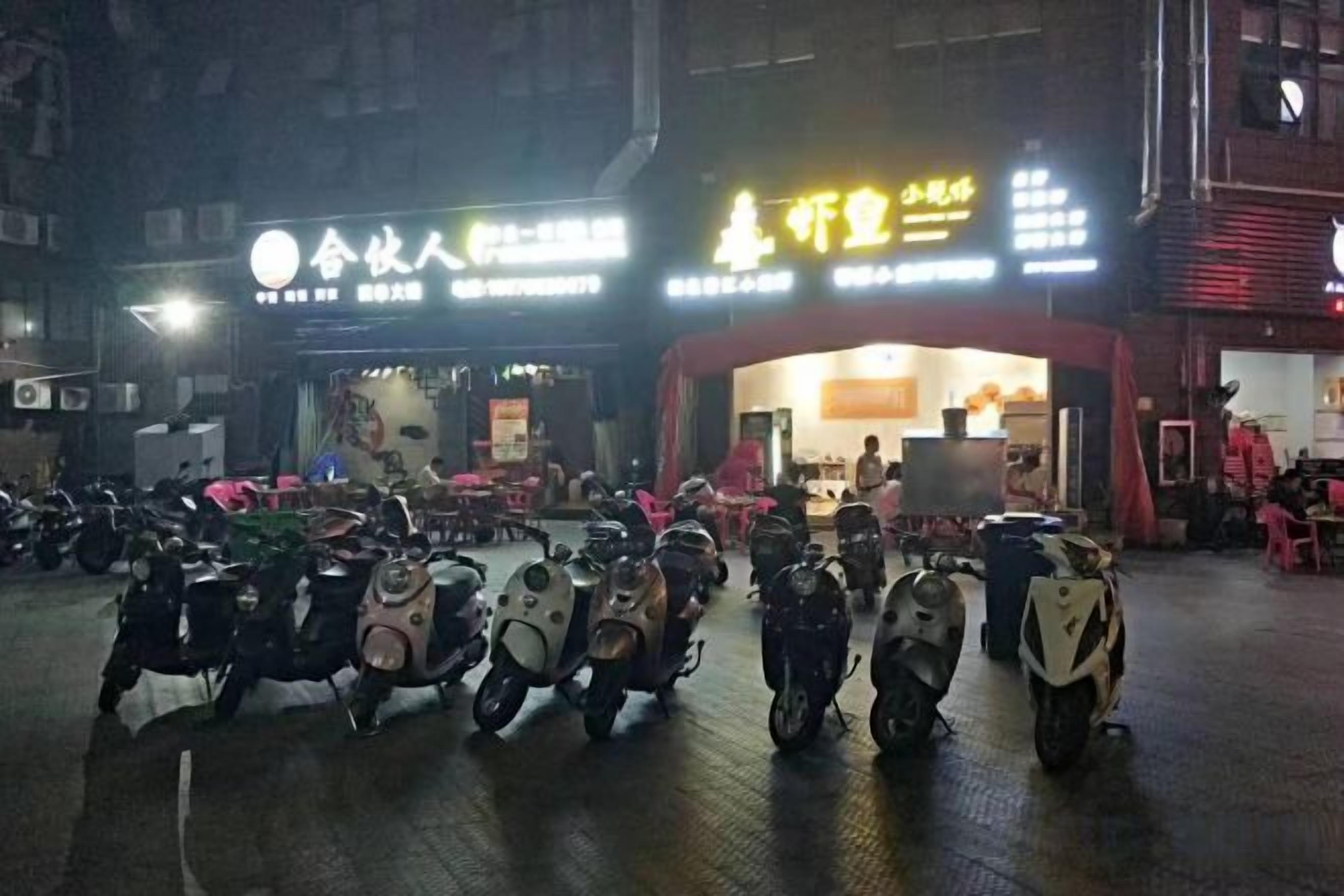 A row of scooters parked in front of a building with illuminated signage.