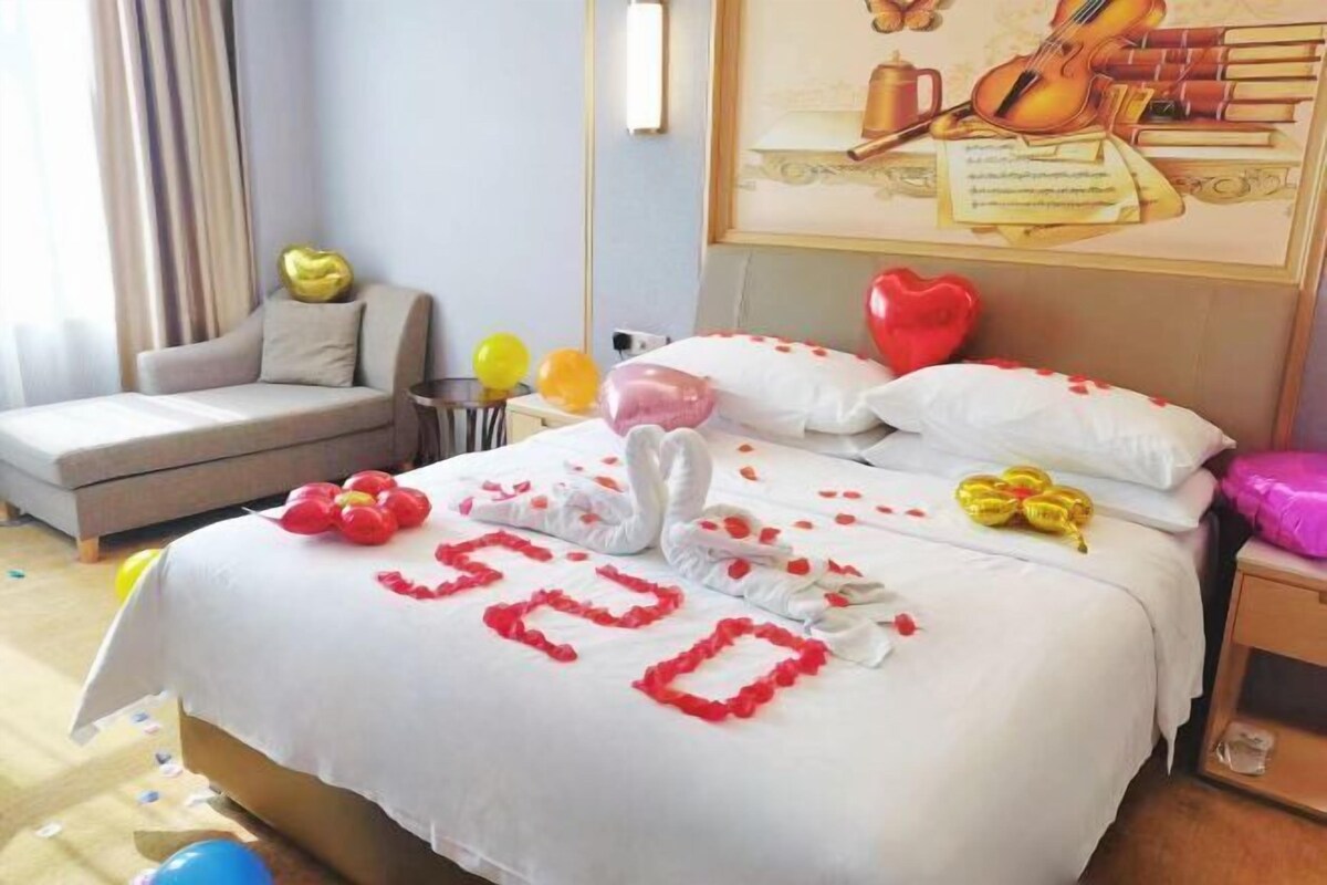 A hotel room with a bed, a sofa, a nightstand, and a wall with a framed picture.