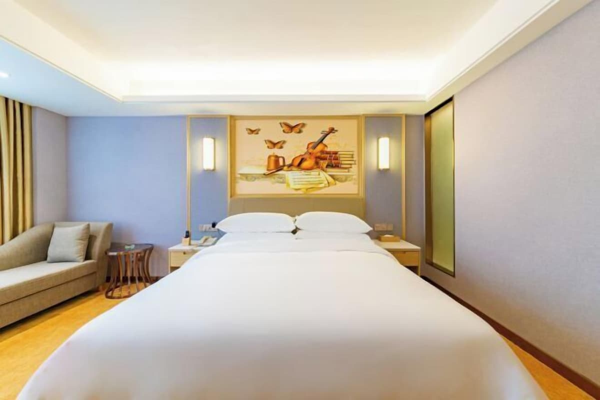 A hotel room with a bed, a sofa, a small table, and a wall with a framed picture.