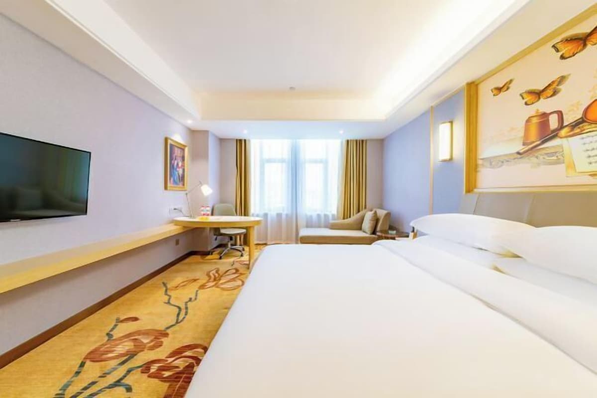 A hotel room with a bed, a desk, a chair, a television, and a window with curtains.