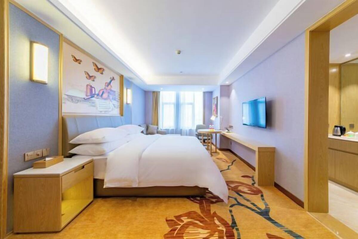 A hotel room with a bed, bedside table, TV, and a large window.