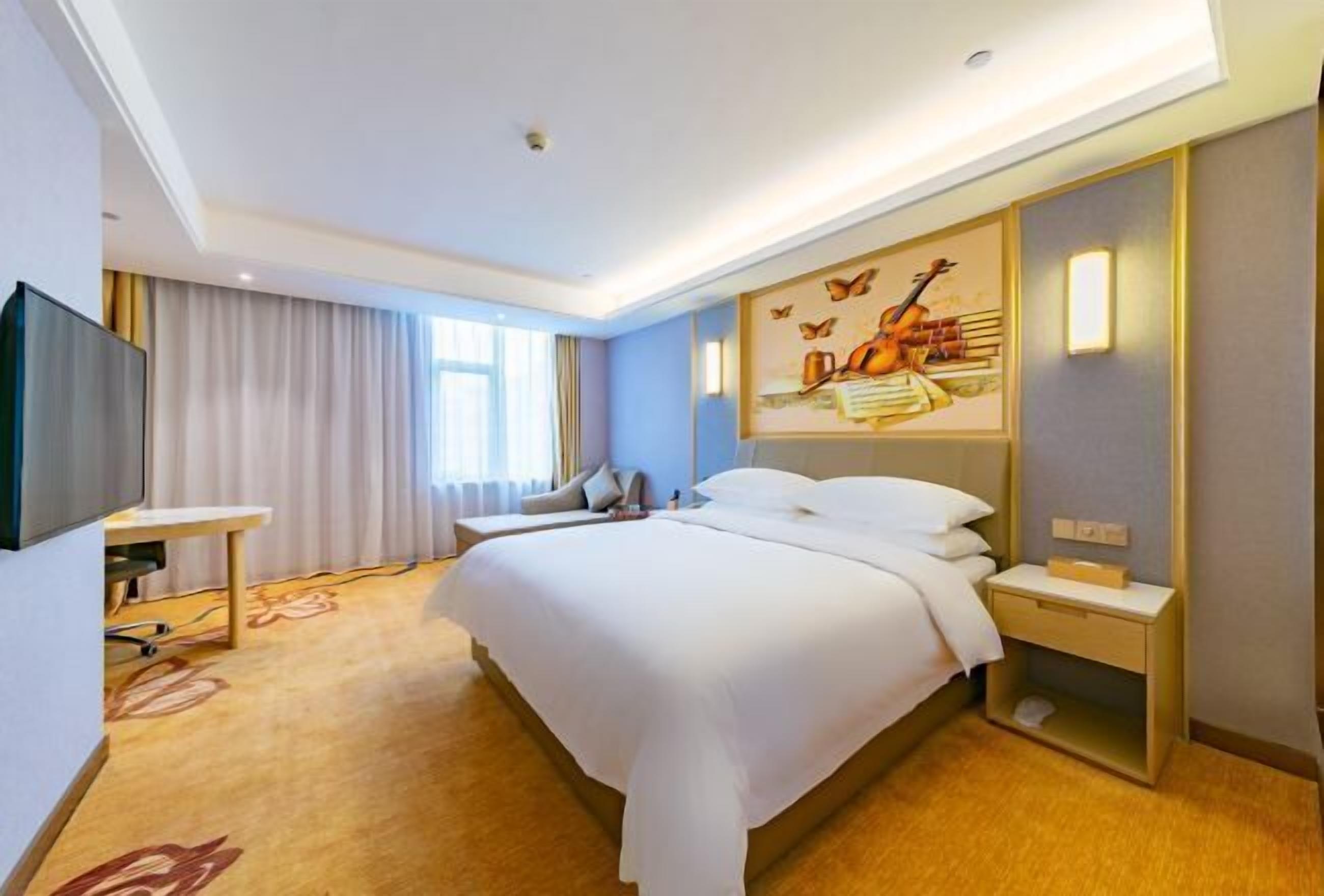 A modern hotel room with a large bed, a flat-screen TV, a desk, and a painting on the wall.