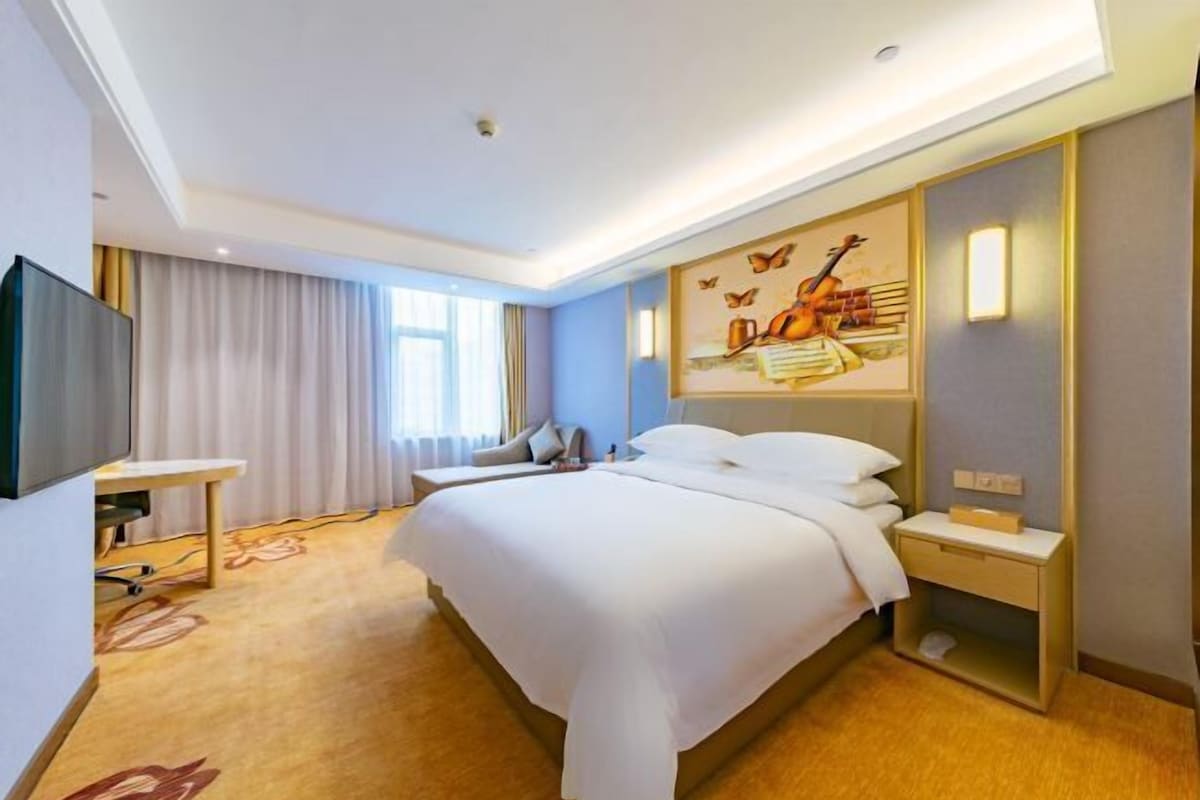 A modern hotel room with a large bed, a flat-screen TV, a desk, and a painting on the wall.