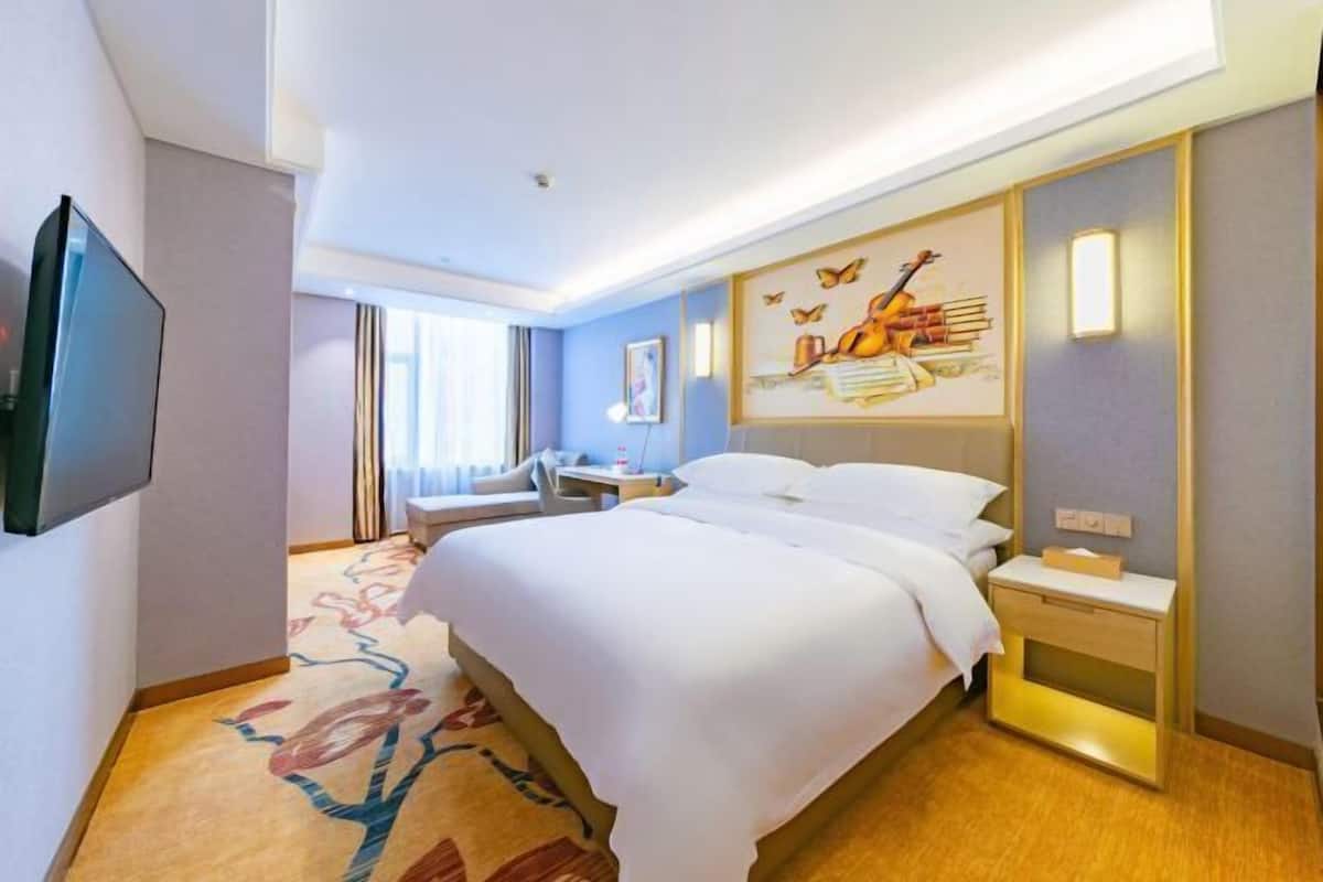 A hotel room with a bed, bedside table, TV, artwork, and a window.