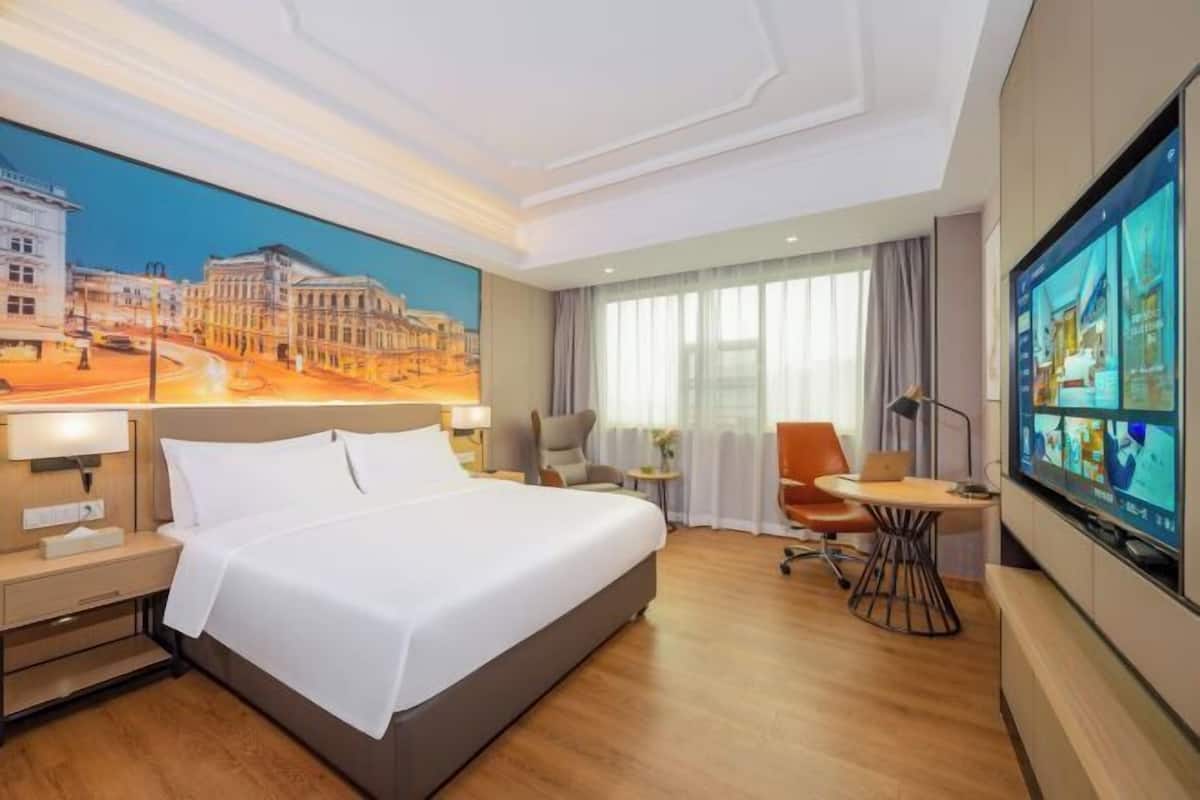 Une chambre d’hôtel avec un grand lit, un bureau avec une chaise, une télévision et un tableau représentant un paysage urbain accroché au mur.
