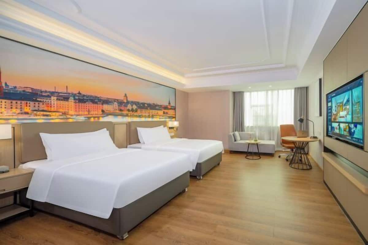 Une chambre d’hôtel avec deux lits, une télévision, un bureau et un tableau représentant un paysage urbain.