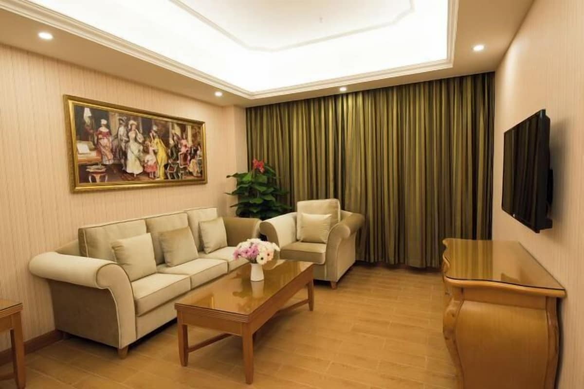 A living room with a sofa set, a coffee table with flowers, a television, and a large painting on the wall.