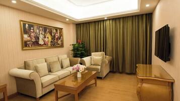 A living room with a sofa set, a coffee table with flowers, a television, and a large painting on the wall.